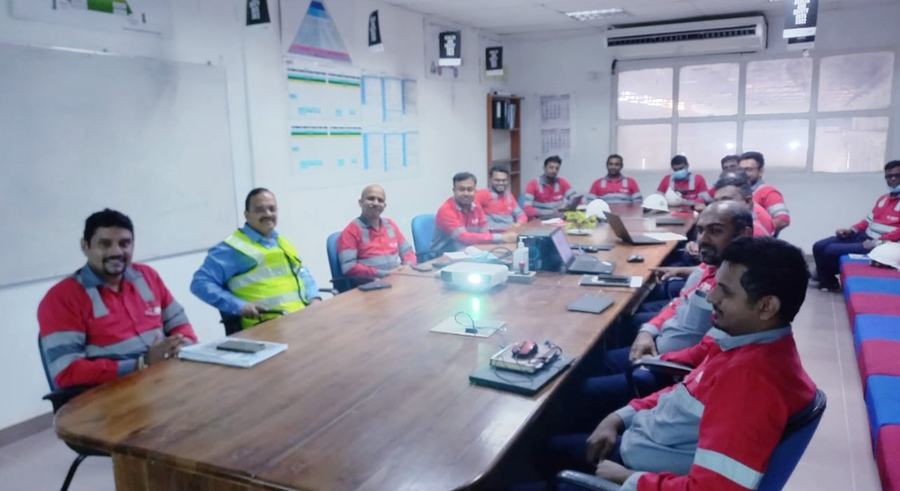 Dr Hegde in a safety vest at a conference table with a plant team in red work uniforms